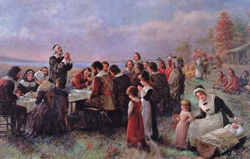 “The First Thanksgiving at Plymouth” by Jennie Augusta Brownscombe, painted in 1914, depicts the Pilgrims and the Wampanoag people gathering around a table full of food from their harvest for the first Thanksgiving dinner.