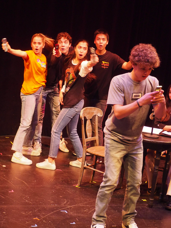 The cast in 21 Chump Street triumphantly display their phones as Justin, the protagonist, realizes it is the key to his immediate dilemma.