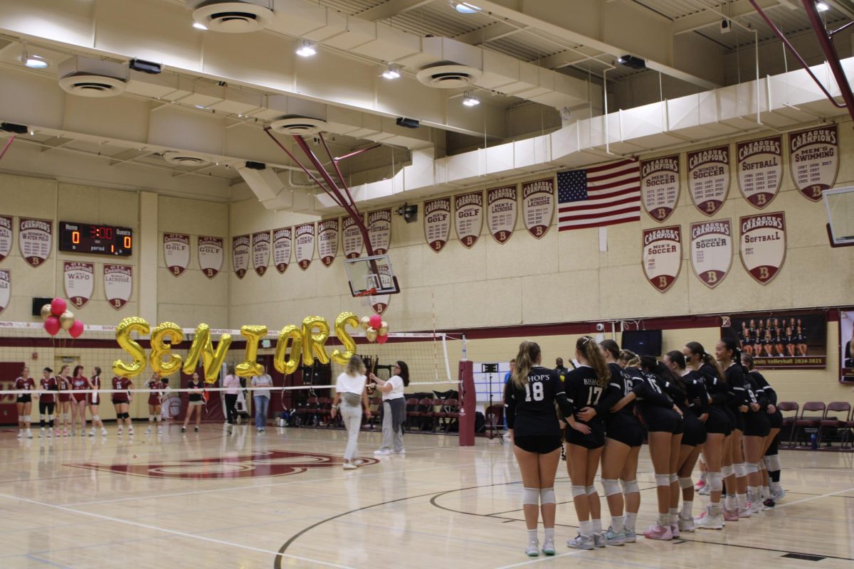 The Girls’ Varsity Volleyball Team lines up in front of the “Senior” balloon letters together to soak it all in before the game begins. 