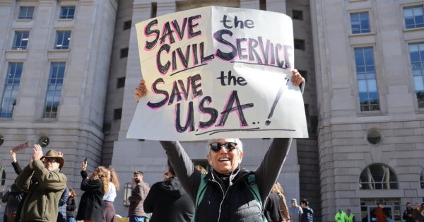 A protester stands outside the United States Agency for International Development (USAID) Headquarters holding a sign that reads “Save the Civil Service, Save the USA.”